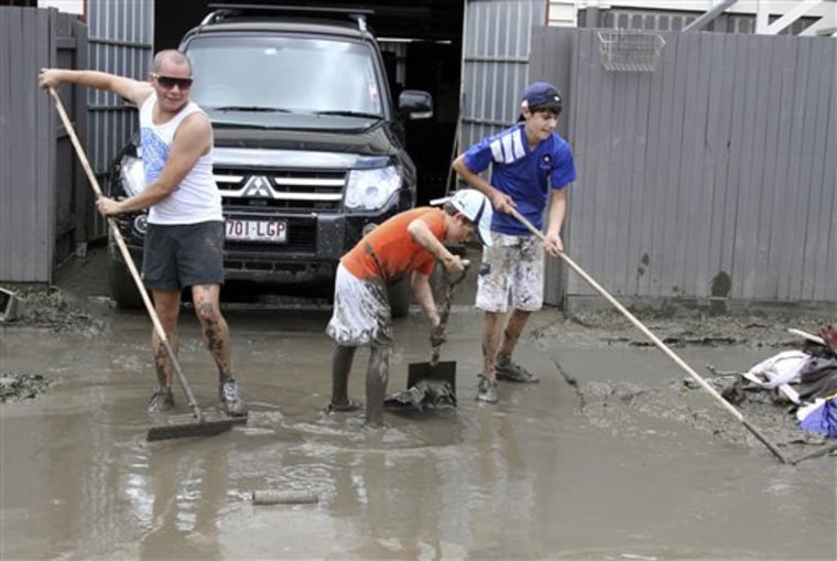 New Farm residents Simon Stapleton, left, and brothers Benjamin, center, 10, and Damian Avenia, right, 14, clear away the mud and debris in front of a home in Brisbane, Australia, Friday, Jan. 14, 2011. Parts of Brisbane reopened as deadly floodwaters that had swamped entire neighborhoods recede, revealing streets and thousands of homes covered in a thick layer of putrid sludge. (AP Photo/Tertius Pickard)